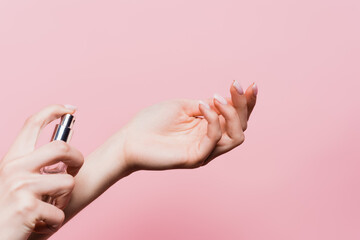 partial view of woman holding bottle and applying luxury perfume isolated on pink