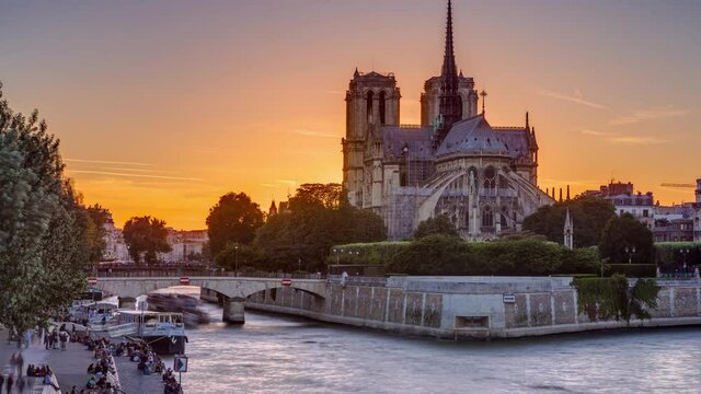 Rear view of Notre Dame De Paris cathedral at sunset with sun in the frame timelapse. View from Tournelle bridge. Orange sky in background. Paris, France, Europe.