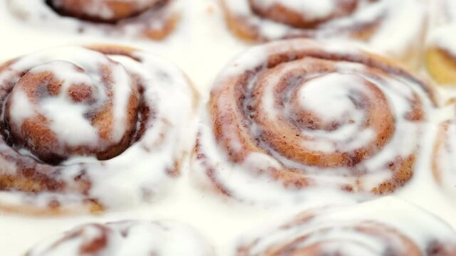 Freshly baked cinnamon rolls with frosting close up, top view. Sweet cream cheese frosting on cinnamon buns. Production of cinnamon rolls. Appetizing cinnamon bun