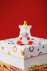 Unicorn figurine on a gift box with gold beads on a red background with free space.