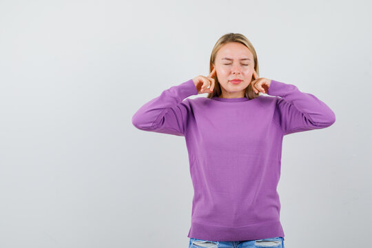  young lady plugging ears with fingers in purple sweater and looking relaxed. front view.