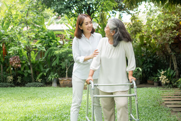 An old elderly Asian woman uses a walker and walking in the backyard with her daughter.  Concept of...