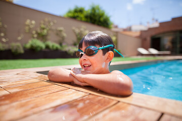 5 year old Caucasian boy with goggles resting on the edge of a garden pool. Cute child having fun on summer vacation.