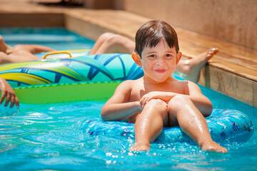 Two caucasian smiling boys, lying on floats, relaxing in a swimming pool. It's a sunny summer day, vacation, holidays.