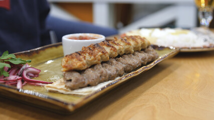 Dinner table served with lula kebabs and fresh vegetables with sauce. People enjoy Armenian style kebab at restaurant.
