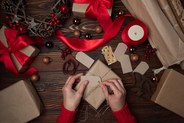 Female hands wrapping gift box on brown wooden table. Top view. New Year or Christmas celebration concept