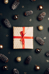 Christmas composition with a gift in a box. Golden toys, modern holiday decorations, gift boxes, fir branches on a dark black background. Elegant Christmas greeting card template.