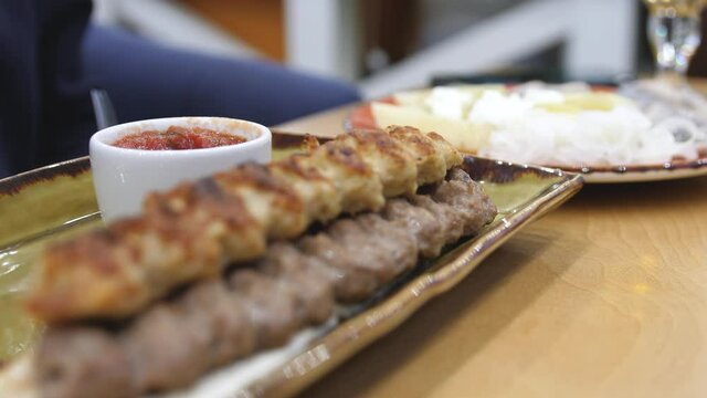 Dinner table served with lula kebabs and fresh vegetables with sauce. People enjoy Armenian style kebab at restaurant.