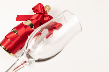 empty wine glass in the foreground against the background of a bottle of champagne wrapped with a red silk ribbon on a white background