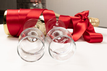 two empty glasses close up and a gift bottle of champagne wrapped in a red silk ribbon on a white background