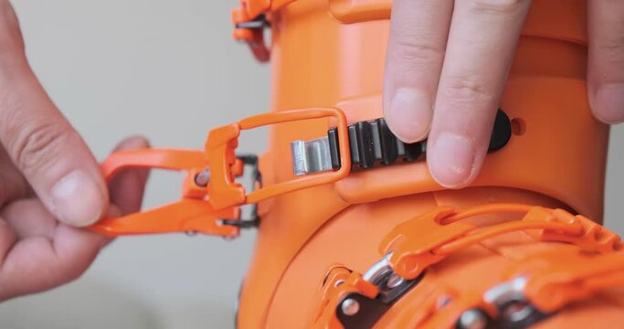 Adjusting boot buckle on orange ski boot - close up of male fingers tightening the boot by one increment, front view. Preparation for skiing, essential ski gear, winter sport.