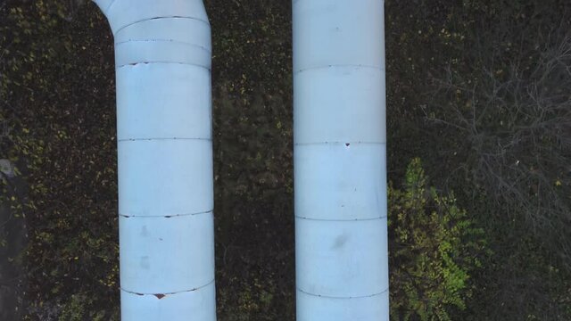 Large pipes of the heating main on a cloudy sunset.
View from above. At the bottom, there are green areas, trees, bushes and grass.