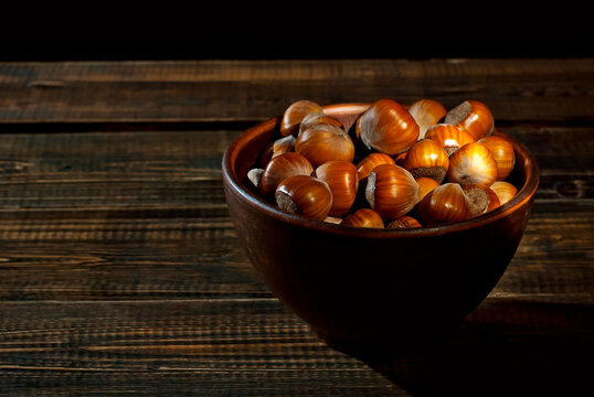 Hazelnuts in a bowl on a brown wooden background. Lots of nuts on an old shabby board. Contrasting dramatic light as an artistic effect. Place for text and copy space near food.