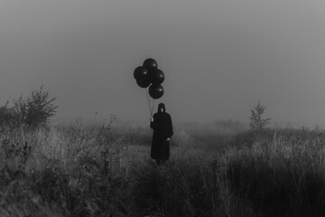 scary dark man in a monster costume with a hood with balloons in his hand
