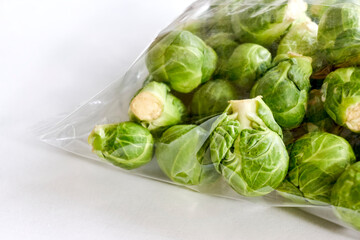 Closeup of green brussels sprouts in transparent plastic package on white background.