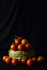 Fototapeta na wymiar Rustic bowl with cherrys tomatoes and more scattered on black cloth, light entering from the side