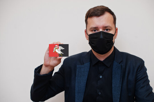 Man wear black formal and protect face mask, hold Buckinghamshire flag card isolated on white background. United Kingdom counties of England coronavirus Covid concept.