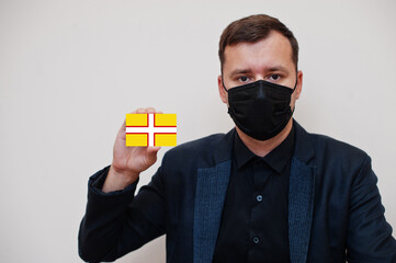 Man wear black formal and protect face mask, hold Dorset flag card isolated on white background. United Kingdom counties of England coronavirus Covid concept.