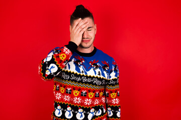 A very upset and lonely Young handsome Caucasian man wearing Christmas sweater against red wall,  crying,