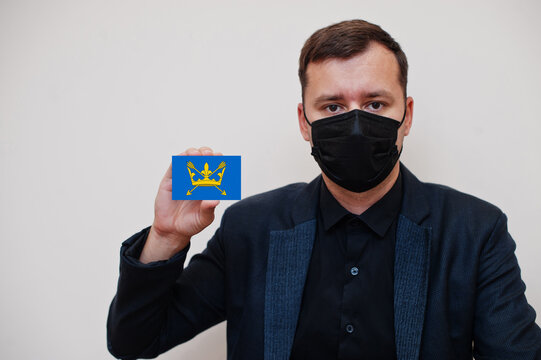 Man wear black formal and protect face mask, hold Suffolk flag card isolated on white background. United Kingdom counties of England coronavirus Covid concept.