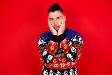 Young handsome Caucasian man wearing Christmas sweater against red wall,  Tired hands covering face, depression and sadness, upset and irritated for problem