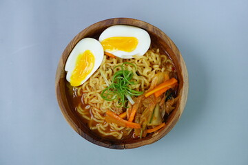 Top view of Ramyeon (Korean instant noodles soup) topped with boiled egg, Kimchi and leek on wooden bowl and chopsticks in stripes napkin and blue background 