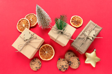 Christmas decorations, gift boxes, dried orange slices, baubles and homemade chocolate chip cookies on red background