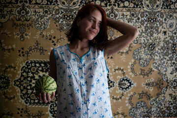 Red Hair Caucasian Girl in Chintz nightgown Sleepwear holding Little Watermelon with the Soviet Carpet on Background