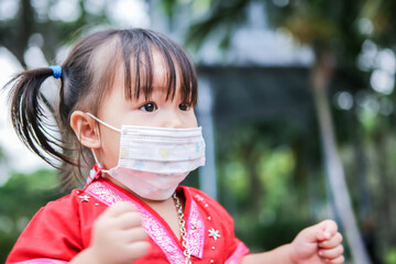 A cute Asian girl wearing a red hill tribe costume, wearing a mask in the playground
