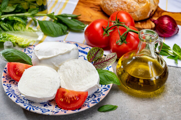 Making of fresh caprese salad with soft Italian cheese from Campania buffalo mozzarella with tomatoes, basil and olive oil
