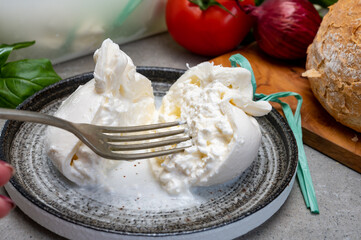 Eating of fresh handmade soft Italian cheese from Puglia, white balls of burrata or burratina cheese made from mozzarella and cream filling
