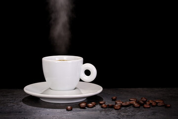 White espresso cup and coffee beans on dark background with copy space.