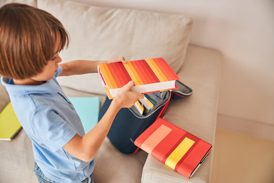 Little boy unpacking his bag and holding books