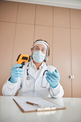 Man in mask and labcoat with a contactless thermometer