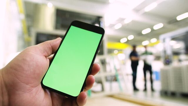 Smartphone in Industrial plant with green screen. Greenscreen smart phone holding in bright industry building with people in background. Iot app 