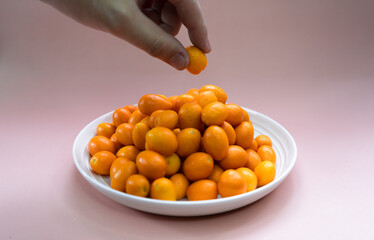 kumquats in white plate on a pale pink background