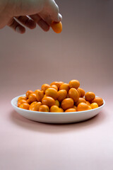 kumquats in white plate on a pale pink background