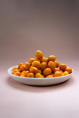 kumquats in white plate on a pale pink background