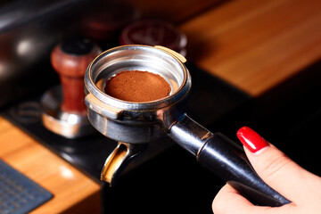 Close-up ground coffee bean in porta filter horn with handle holding by woman hand. Coffee making...
