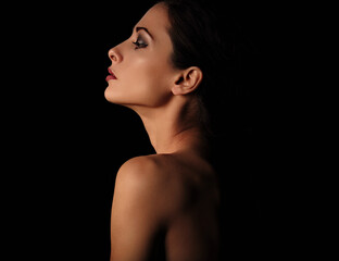 Beautiful mysterious woman in darkness with healthy neck, shoulders and serious wisdom look on dramatic  black background with empty copy space. Closeup portrait. Profile view.