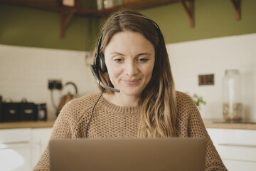 Female using headset during video call, working from home at kitchen table