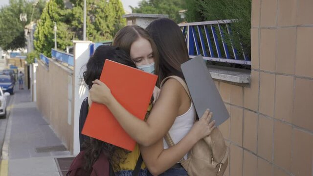 University girls hug each other when they meet again after quarantine. Young women wearing masks return to university