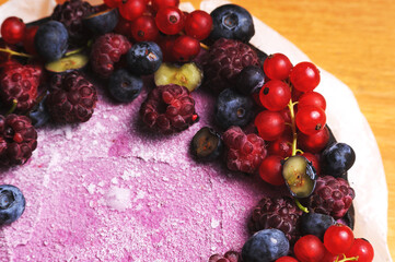 Festive cake, blueberry and blackberry sponge cake with cream cheese inside on a plate on a wooden table, horizontal view from above.Macro photo.