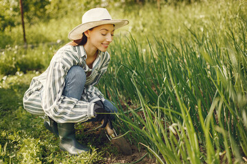 Naklejka na ściany i meble Young woman harvesting fresh seedlings. Lady in a hat. Girl in a garden.