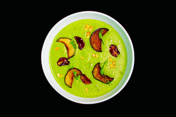 Close-up of cream spinach green soup with dried fruits and peanuts in a deep plate