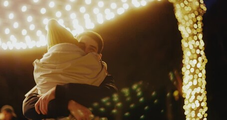 Young woman meeting up with boyfriend on birthday christmas evening party hugging tightly together swinging on the street. Illumination. Beautiful love couple.