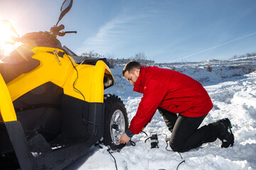 Young man checking air pressure in wheels on the ATV quad bike stand in heavy snow.