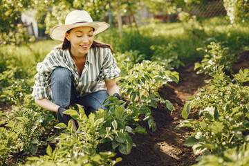 Young woman harvesting fresh seedlings. Lady in a hat. Girl in a garden.