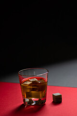 Whiskey and whiskey stones in a glass on a red and black background. Minimalistic composition. Copy space