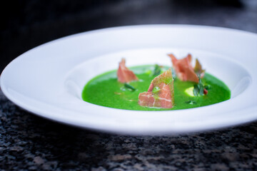 closeup of cream spinach soup with bacon on gray marble on a white plate